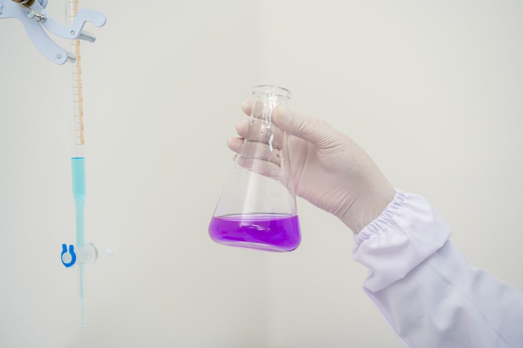 An analyst’s hands holding a purple flask in a white lab — Company Profile, PT Dwi Jaya Cosmedika
