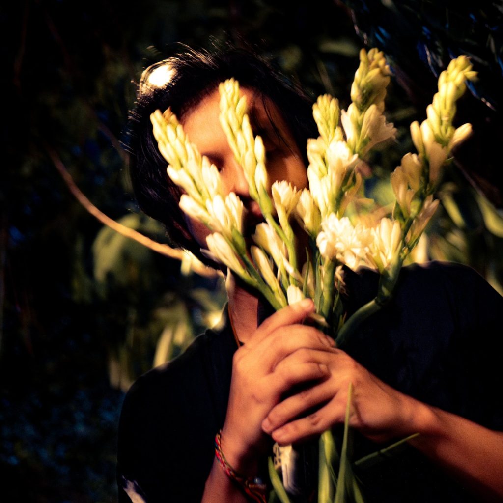 Performer with tuberose flowers, low-key light — Rihlah Bisma live at Kedai Nyamin (music performance)